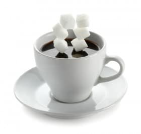 A cup of coffee with sugar cubes falling in