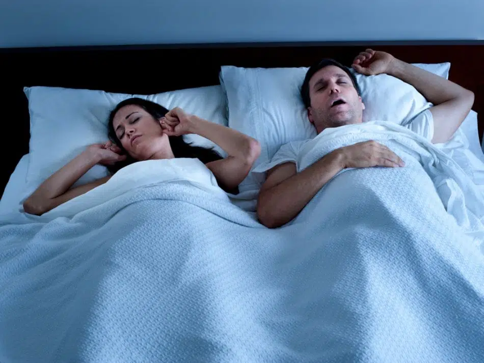 couple-laying-in-bed-man-snoring-woman-plugging-ears