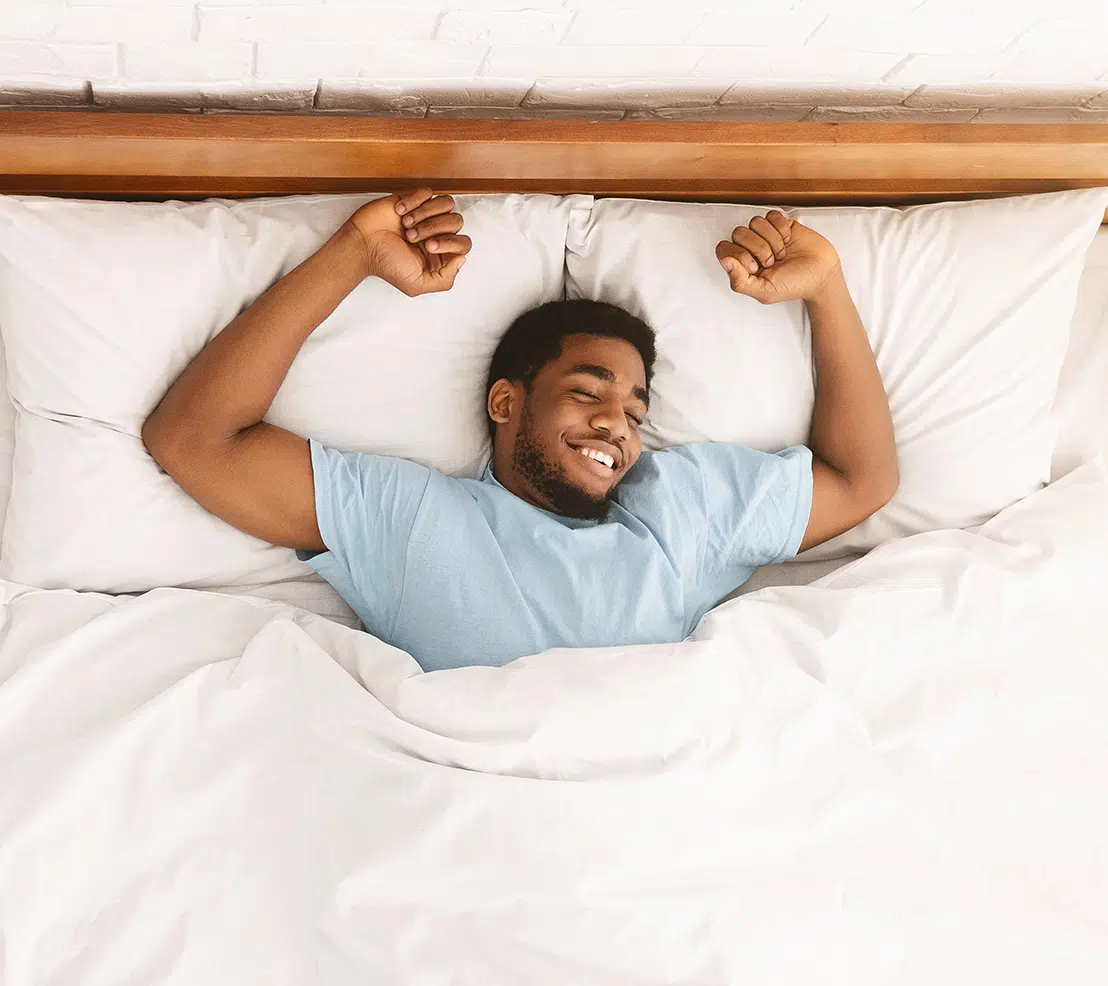 Financing and Insurance Content A man in a light blue shirt smiles while stretching in bed, covered by a white blanket.