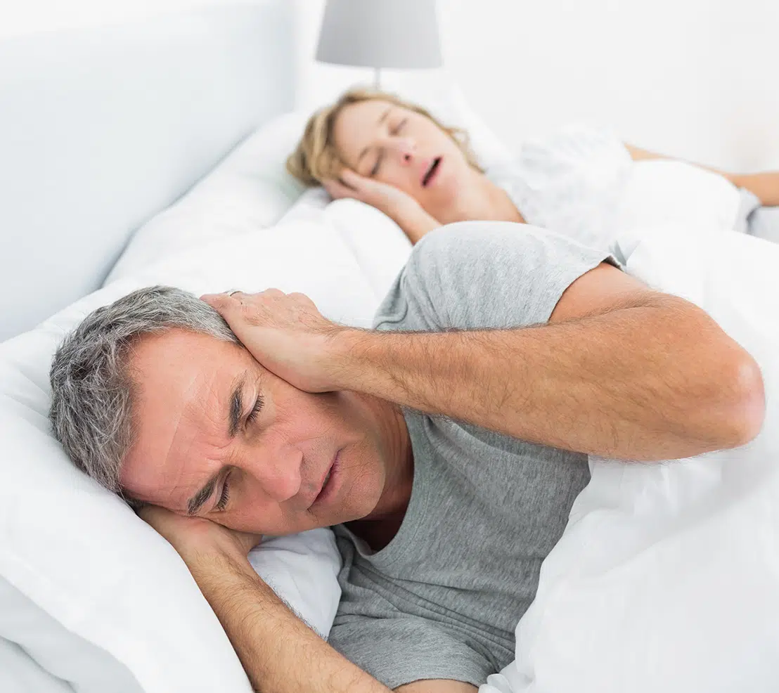 Frustrated man covering his ears while his partner snores